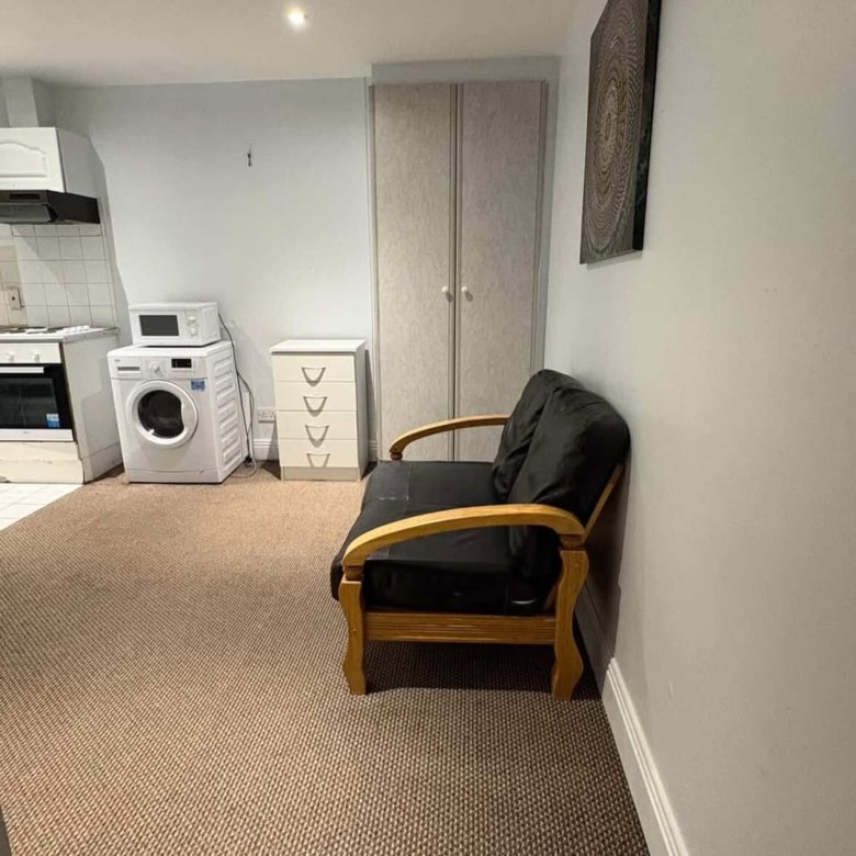 Studio apartment with washing machine, microwave, small sofa, drawers, and wardrobe. Neutral color scheme.