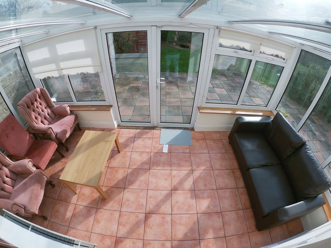 Sunroom with pink armchairs, black sofa, and tile flooring. Bright, airy space.
