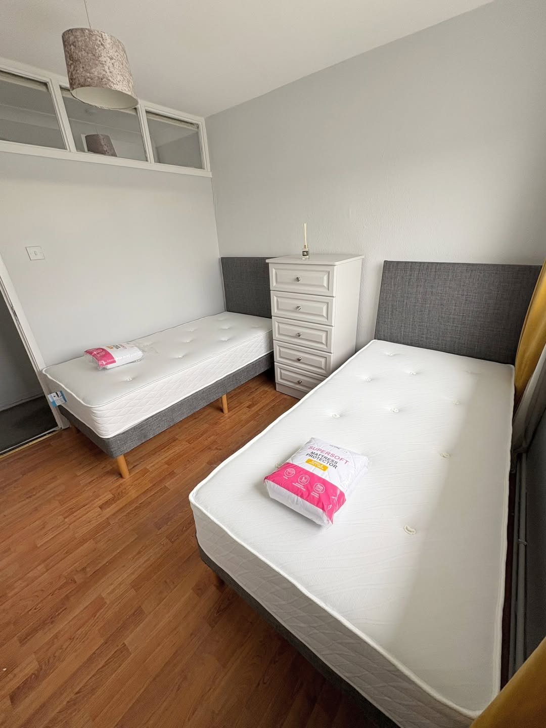 Twin bedroom with two beds, dresser, and wooden floor.