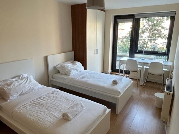 Twin bedroom with white beds, desks, and a window view.