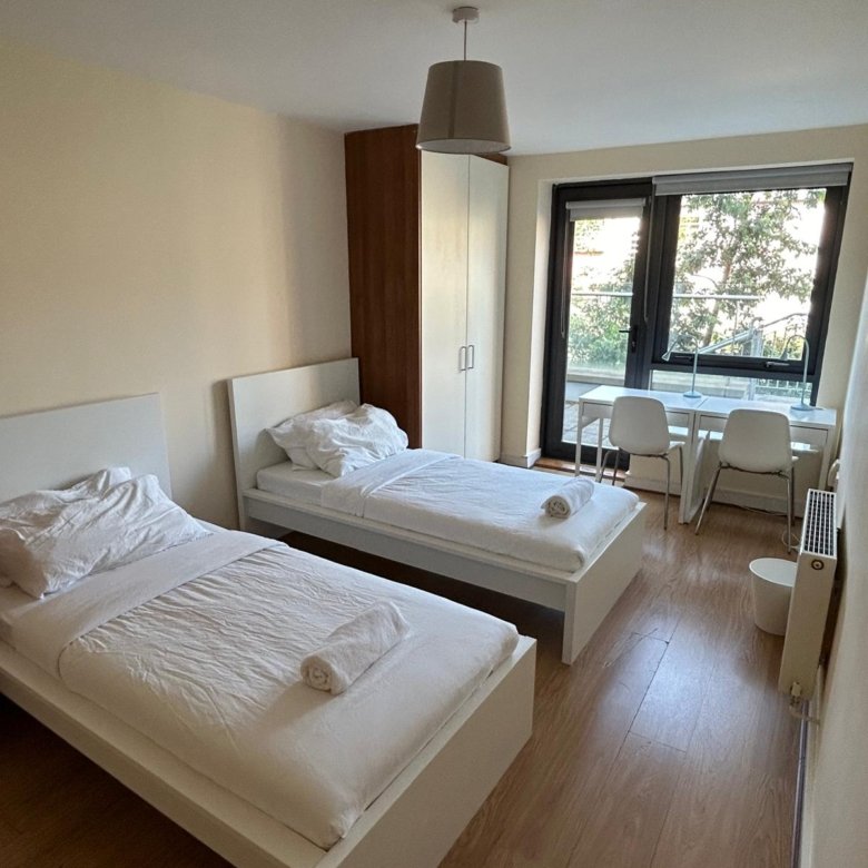 Twin bedroom with white beds, desks, and a window view.