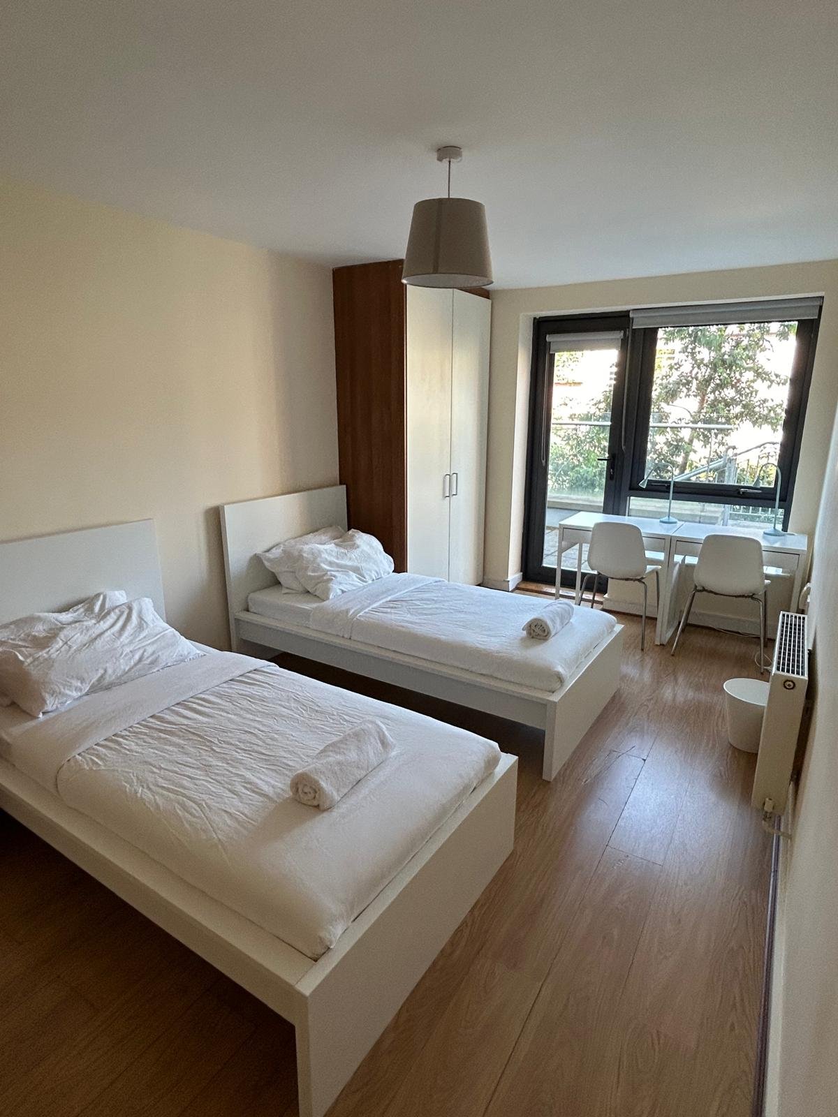 Twin bedroom with white beds, desks, and a window view.