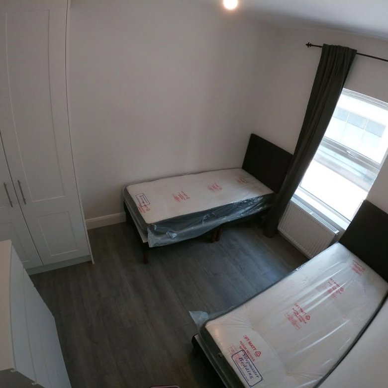 Bedroom with two twin beds, wardrobe, and grey wood floor.