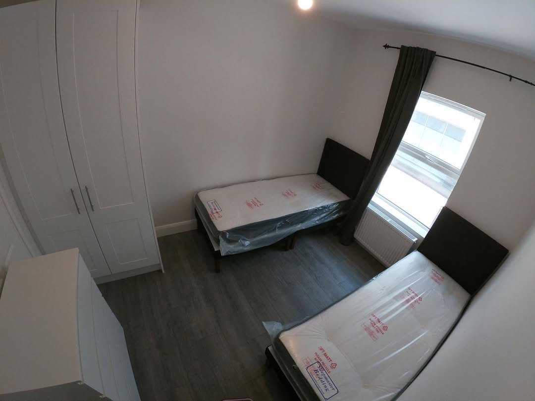 Bedroom with two twin beds, wardrobe, and grey wood floor.