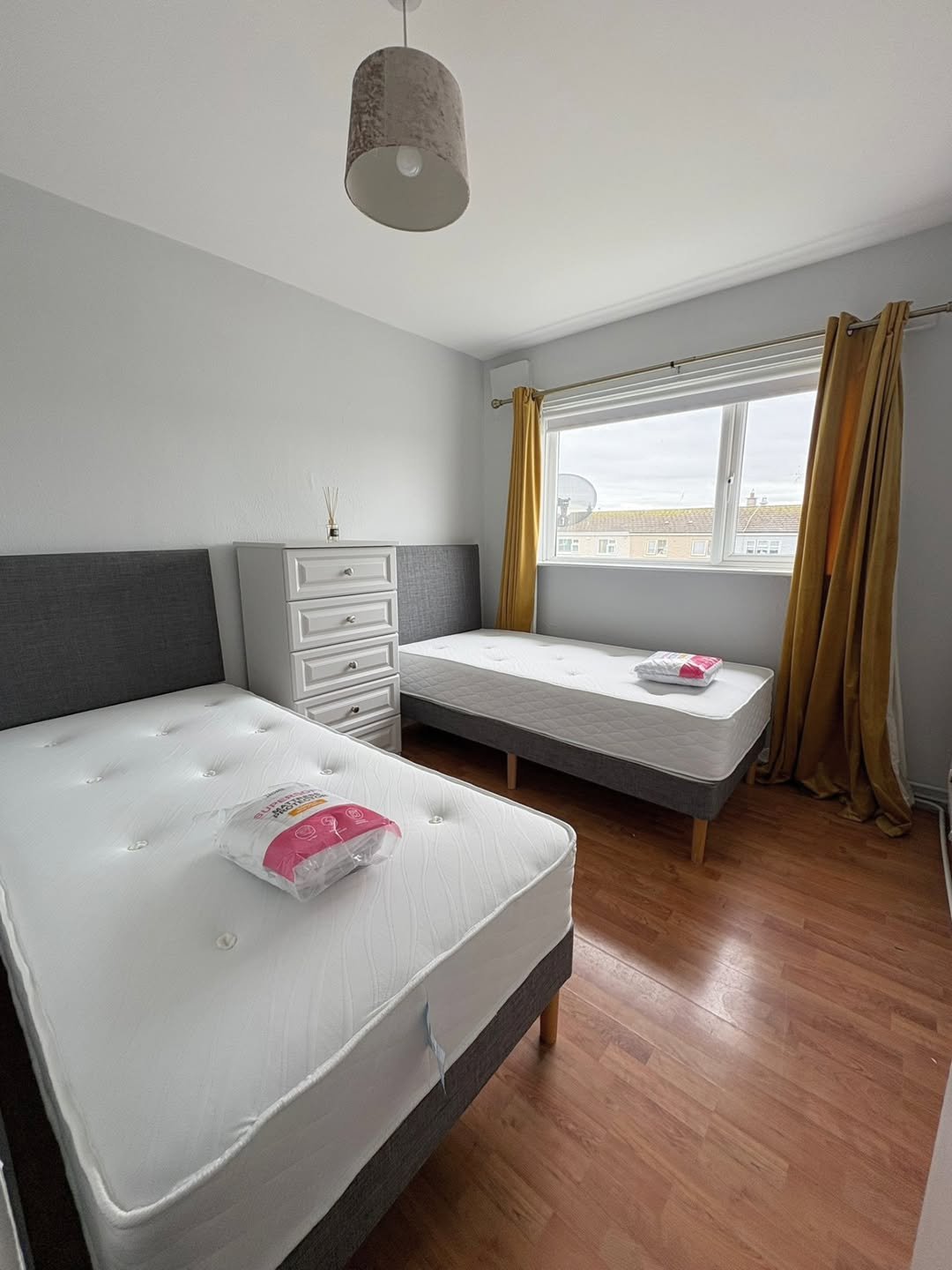 Bedroom with two twin beds, white dresser, and golden curtains.