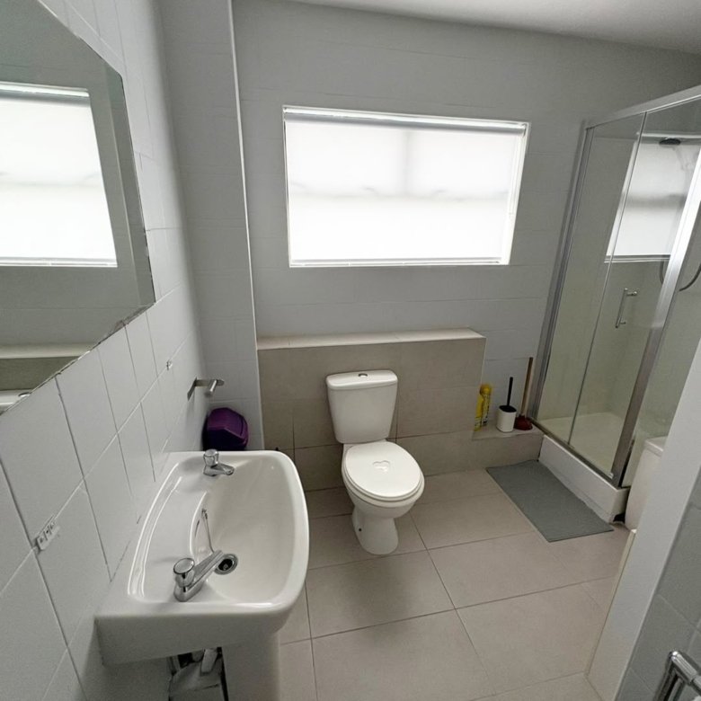 Bathroom with white toilet, sink, shower, and neutral tile flooring.