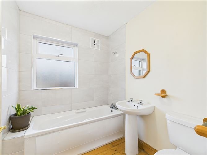Bathroom with white tub, sink, toilet, window, and wooden floor.
