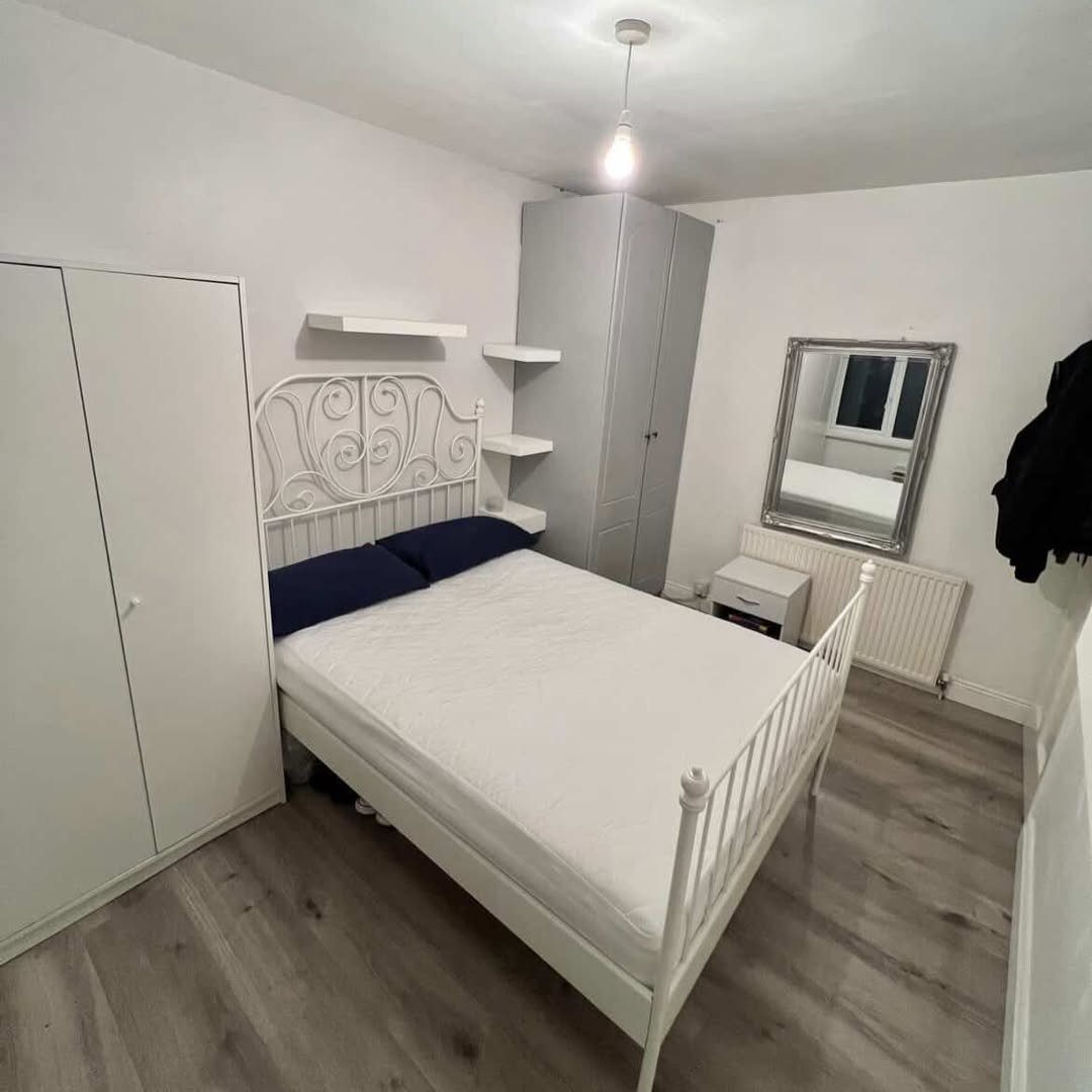Bedroom with white metal bed, grey wardrobe, and silver mirror.