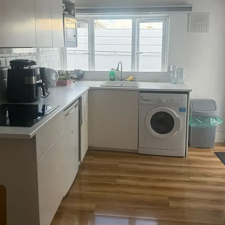 Bright white kitchen with washing machine, sink, and window.