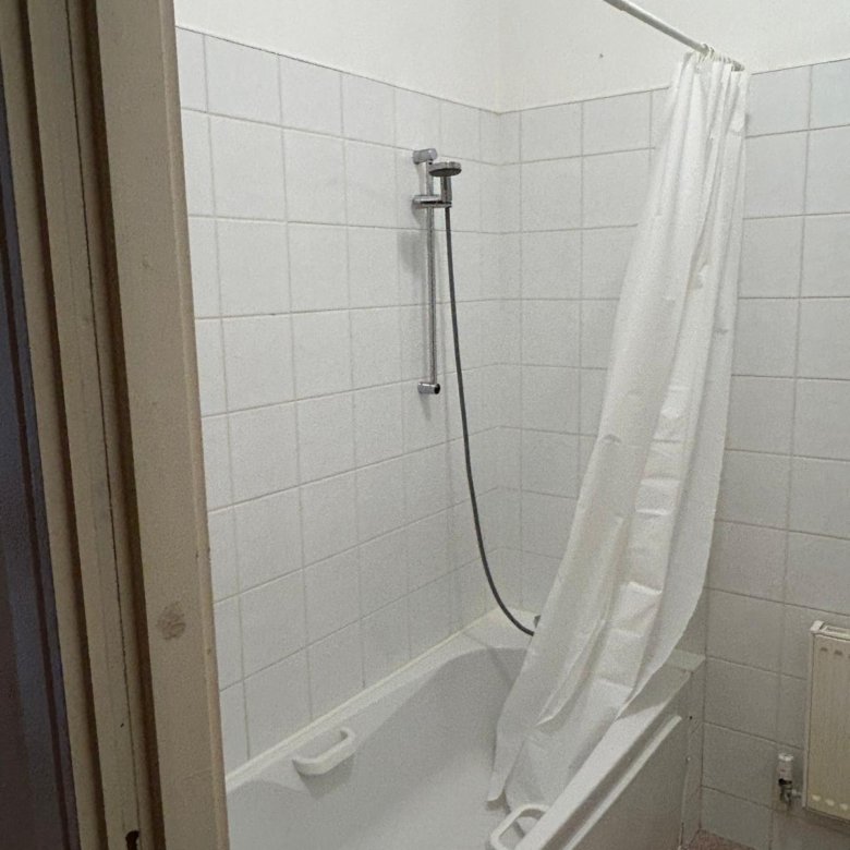 Bathroom with white tile, bathtub, shower head, and shower curtain.