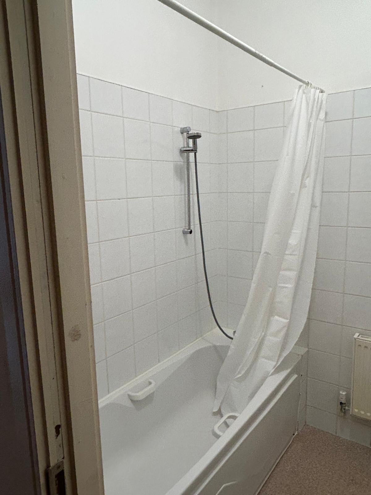 Bathroom with white tile, bathtub, shower head, and shower curtain.