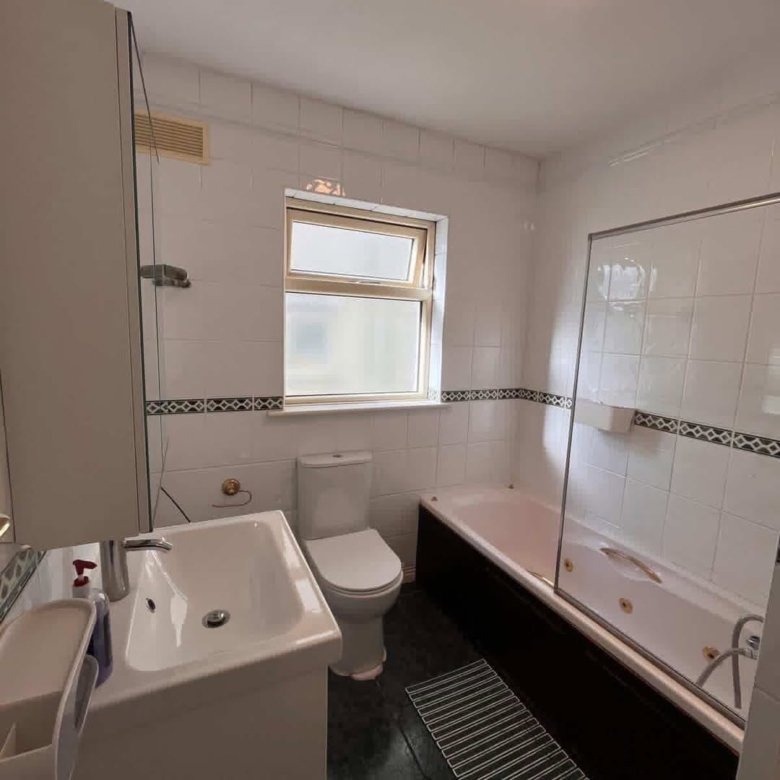 Bathroom with white tiles, dark brown tub, toilet, sink, and window.