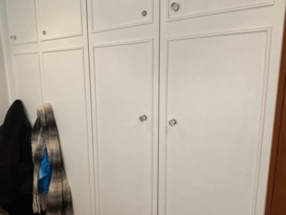 White wardrobe with crystal knobs and clothes hanging beside it.