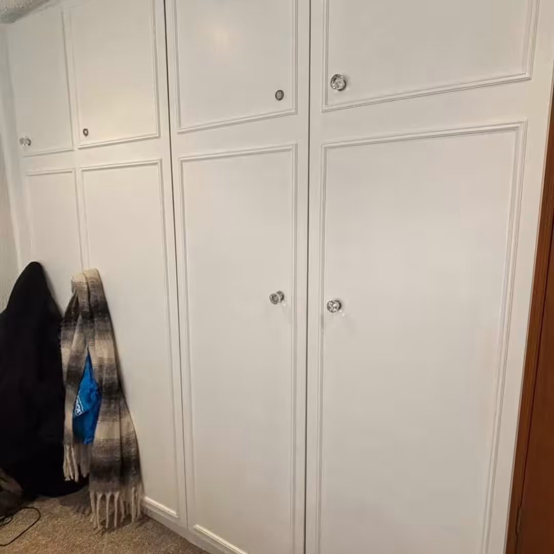 White wardrobe with crystal knobs and clothes hanging beside it.