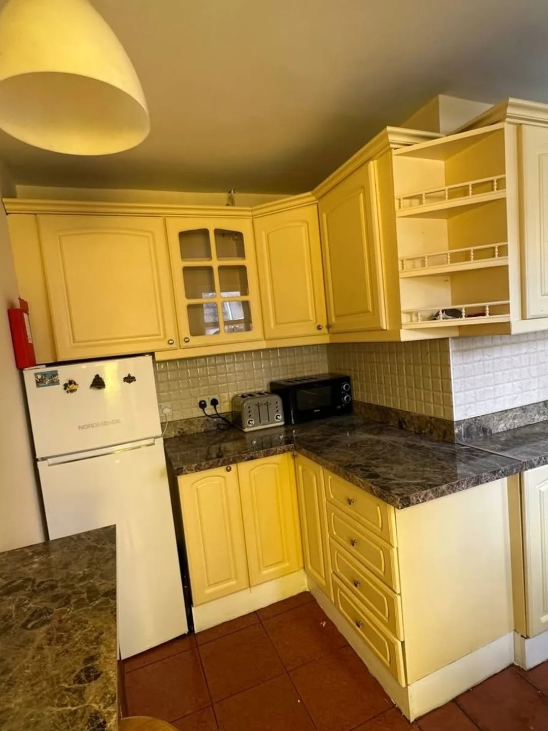 Yellow kitchen cabinets with marble countertop, refrigerator, and appliances.