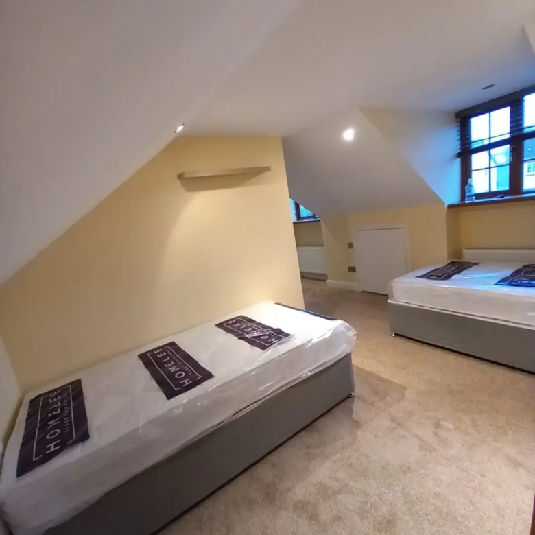 Attic room with two single beds, yellow walls, and a window.