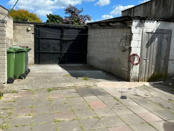 Backyard with bins, gate, shed, and paving stones under a blue sky.
