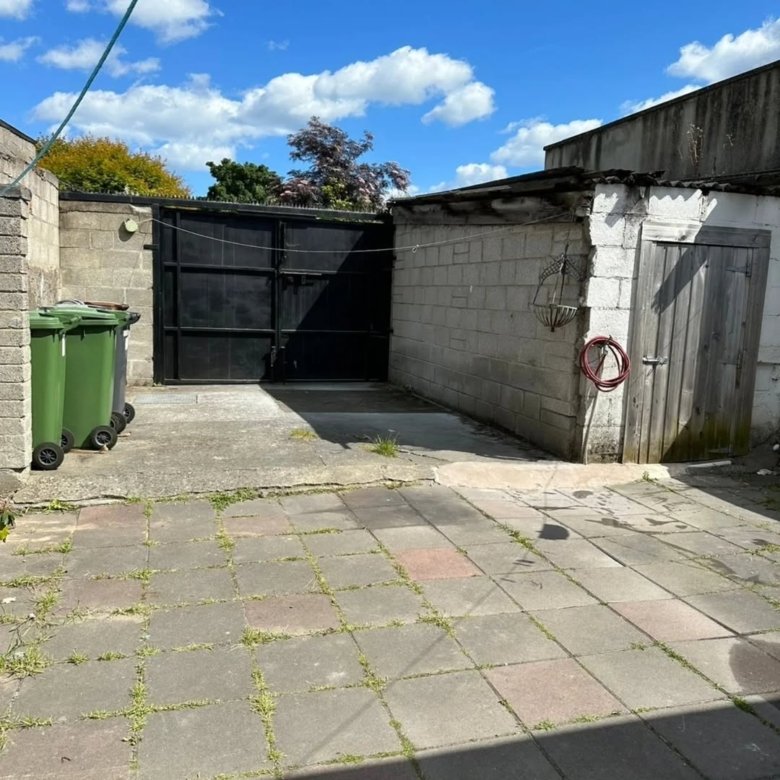 Backyard with bins, gate, shed, and paving stones under a blue sky.