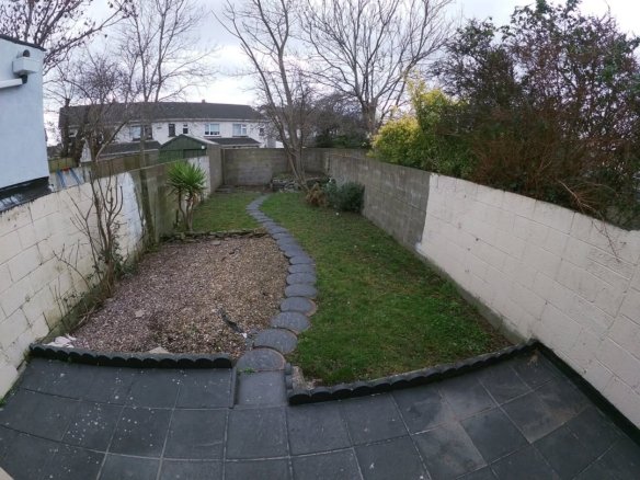 Backyard with stone path, grass, gravel, and concrete walls on a cloudy day.