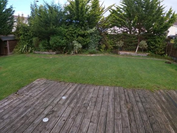 Backyard with wooden deck, green lawn, and trees in background.