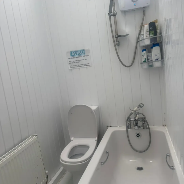 Bathroom with toilet, bathtub, shower, and a sign in Portuguese.