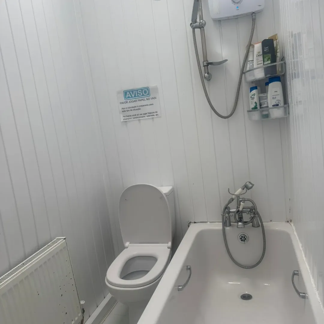 Bathroom with toilet, bathtub, shower, and a sign in Portuguese.