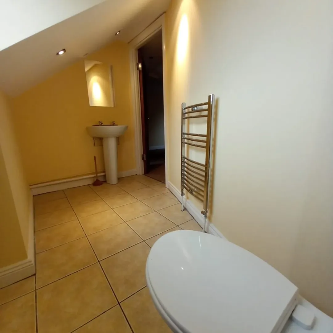 Bathroom with toilet, sink, towel warmer, and yellow walls under sloped ceiling.