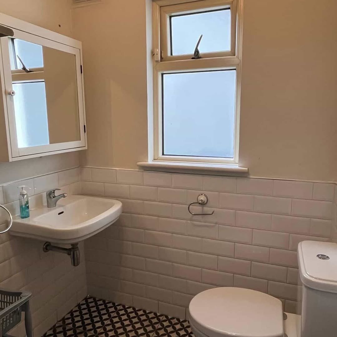 Bathroom with white subway tile, patterned floor, toilet, sink, medicine cabinet, and frosted window.