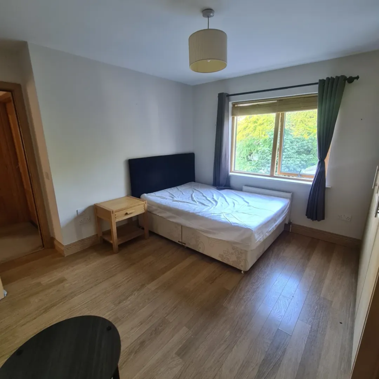 Bedroom with bed, nightstand, window, and wood floor. Simple, clean interior design.