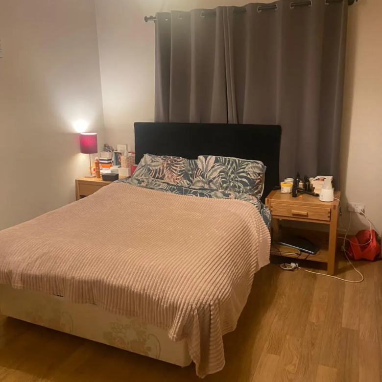 Bedroom with bed, nightstands, gray curtains, and pink blanket. Cozy interior.