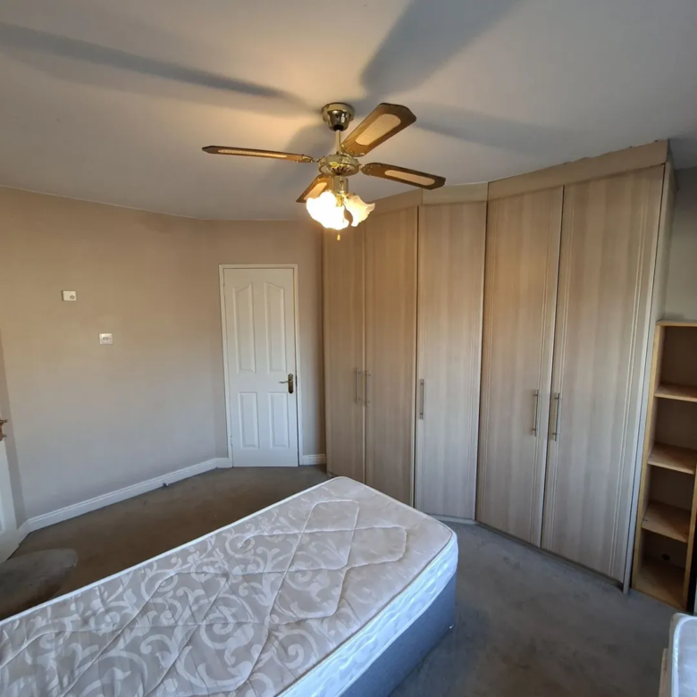 Bedroom with bed, wardrobe, ceiling fan, and neutral color scheme.