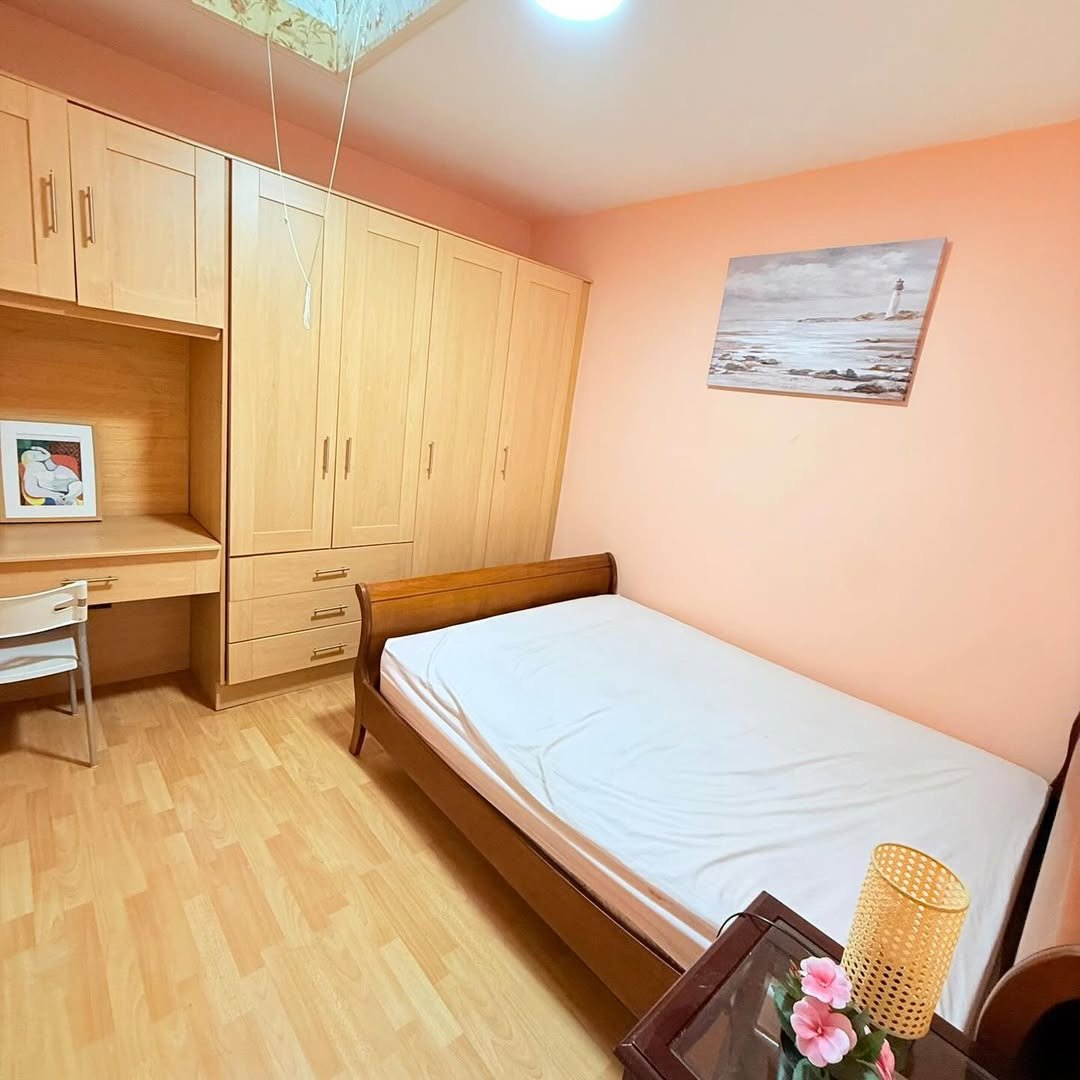 Cozy bedroom with bed, built-in wardrobe, desk, and seaside artwork.