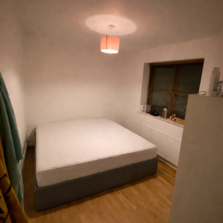 Bedroom with bed, window, light fixture, and wardrobe. Neutral decor.