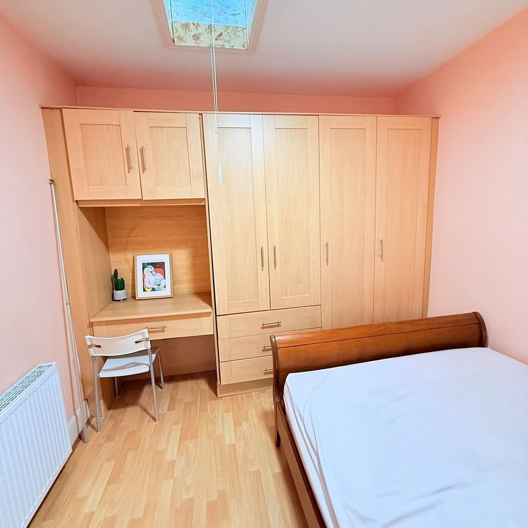 Bedroom with built-in wardrobe, desk, bed, and pink walls.