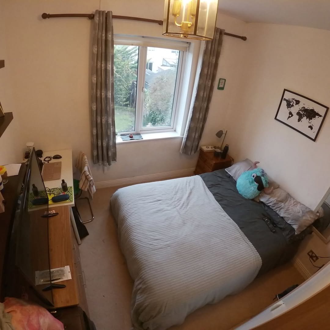 Bedroom with double bed, window, desk, and world map on the wall. Neutral color scheme and simple decor.