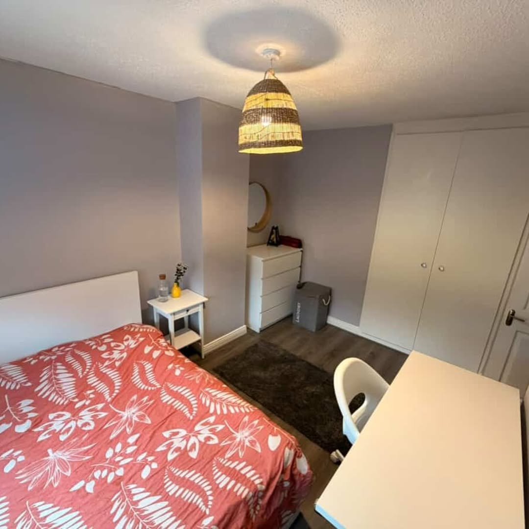 Cozy bedroom with bed, desk, wardrobe, and natural light from a woven lamp.