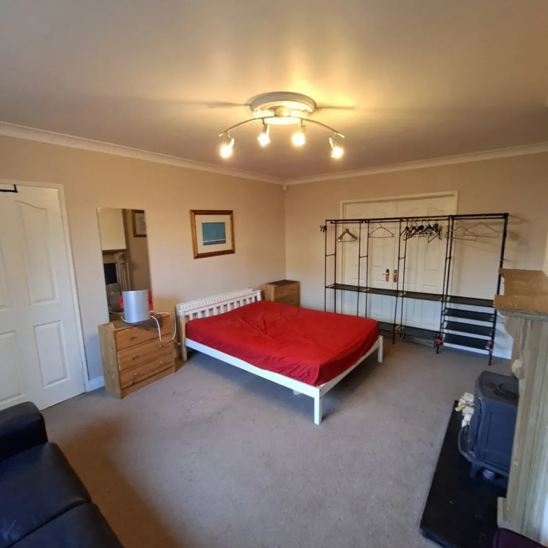 Bedroom with red bedspread, white frame, wardrobe, dresser, and fireplace. Neutral color scheme.