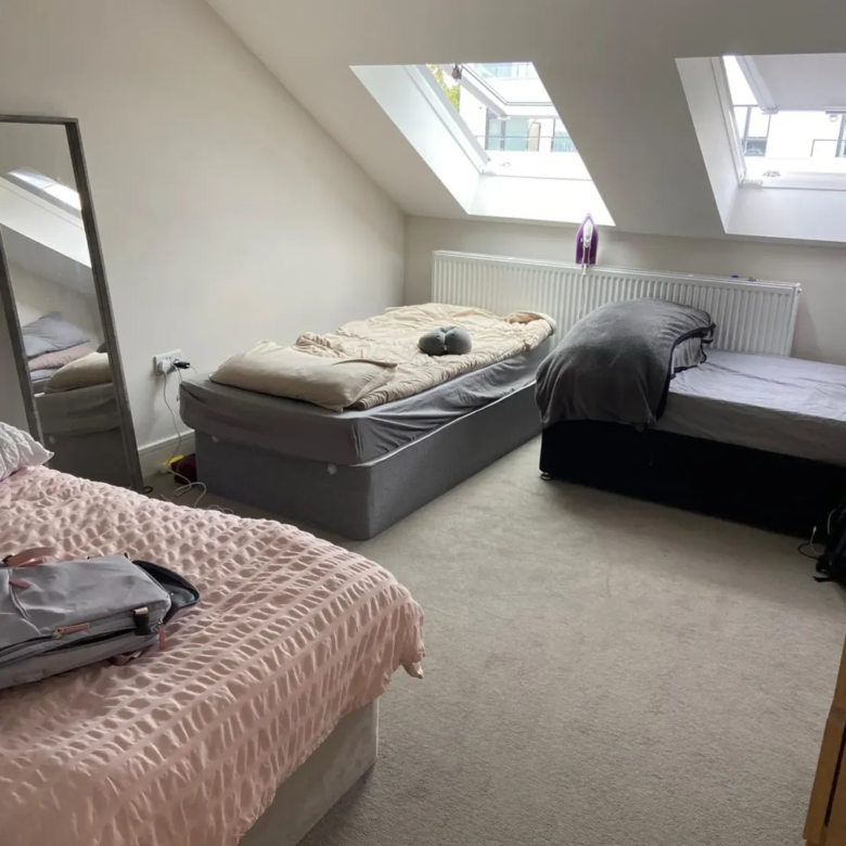 Bedroom with three beds under attic windows, mirror on the side.