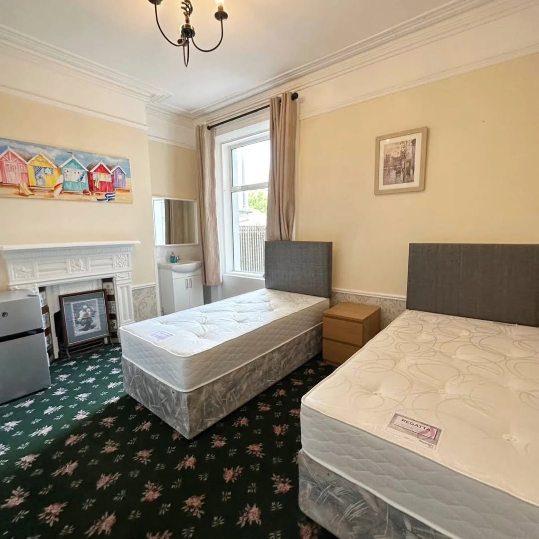 Bedroom with two twin beds, floral carpet, decorative fireplace, and beach hut art on the wall.