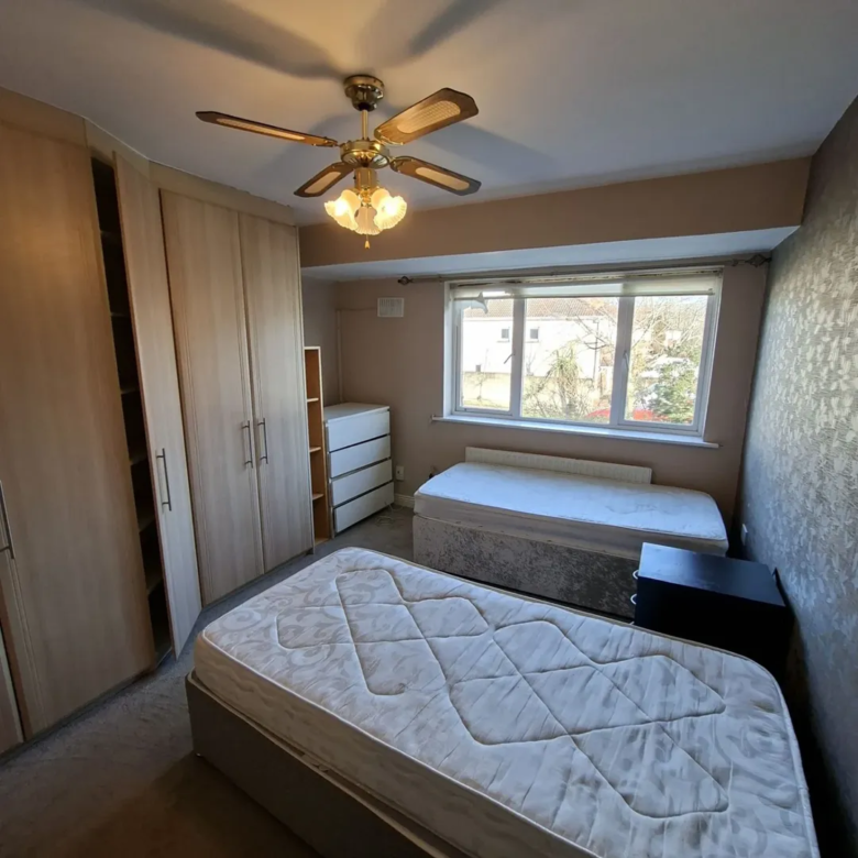 Bedroom with twin beds, wardrobes, ceiling fan, and window overlooking greenery.