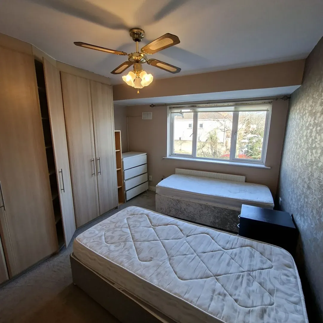 Bedroom with twin beds, wardrobes, ceiling fan, and window overlooking greenery.