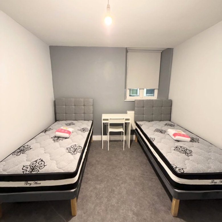 Bedroom with two beds, desk, and grey accent wall. Neutral color scheme.