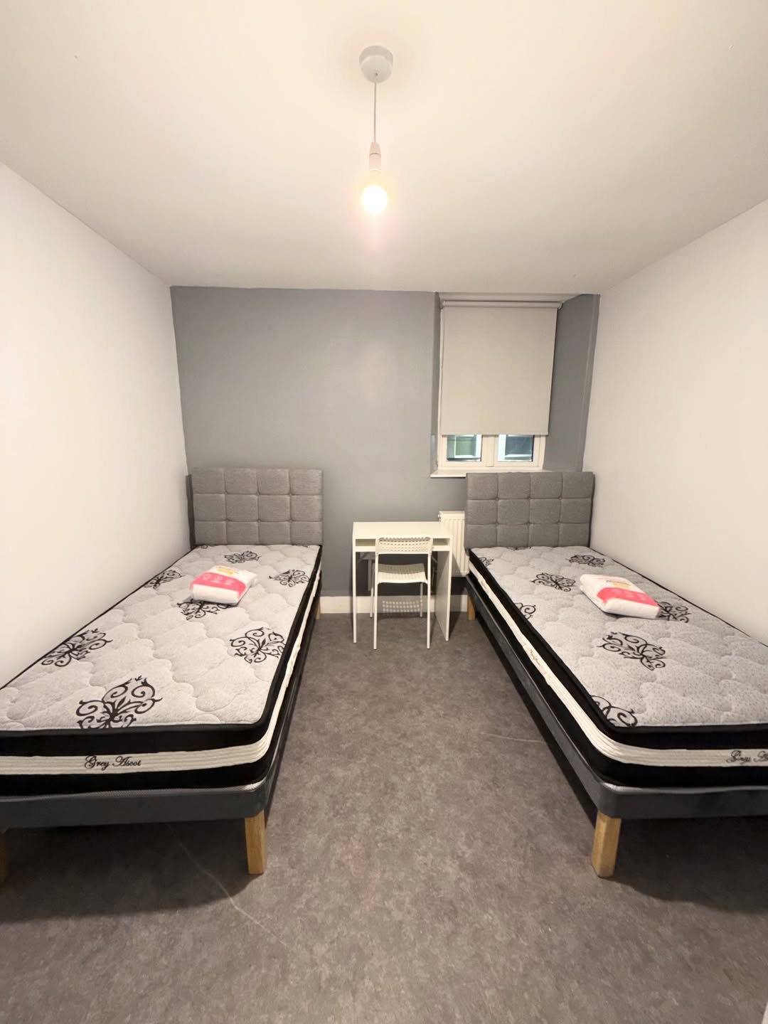 Bedroom with two beds, desk, and grey accent wall. Neutral color scheme.