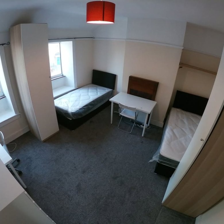 Bedroom with two single beds, desks, wardrobes, and a red lampshade. Window provides natural light.