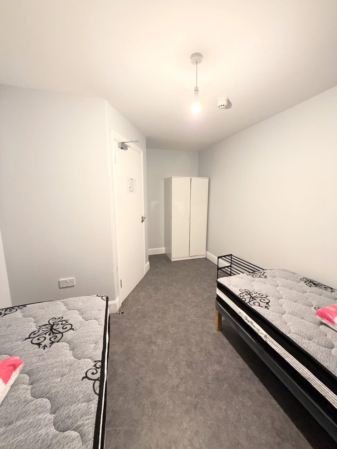 Bedroom with two single beds, wardrobe, and white door. Minimalist interior design with gray carpet.