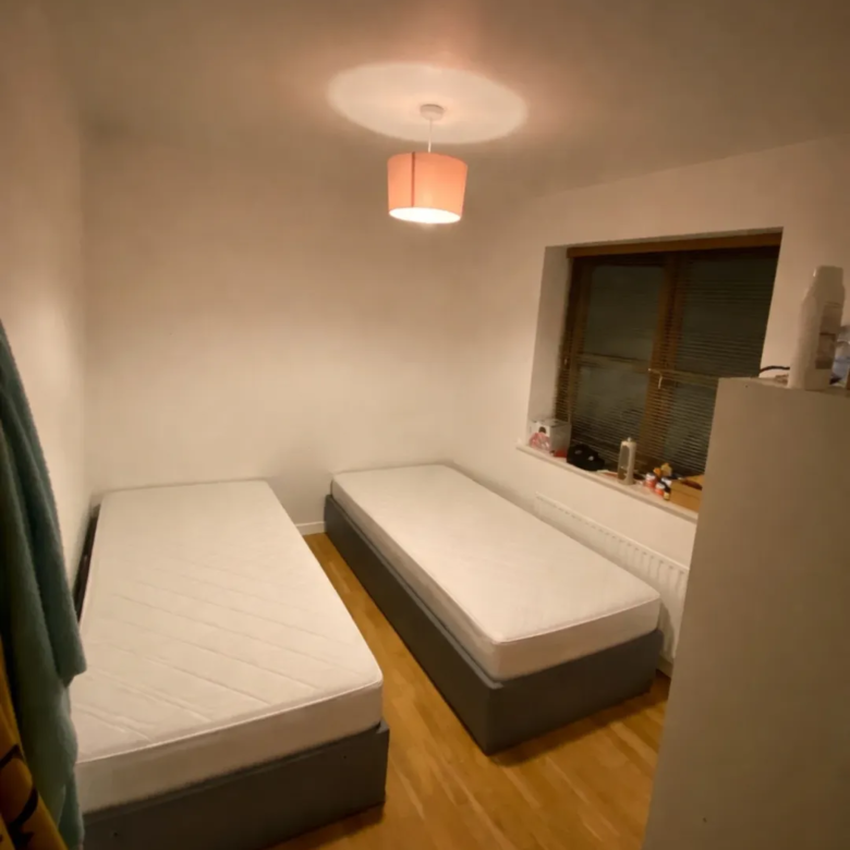 Cozy bedroom with two single beds, light wood floor, and warm lighting.