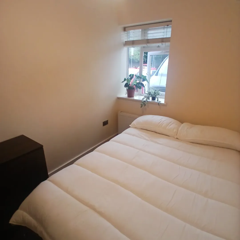 Cozy bedroom with white bedding, plants on windowsill, natural light.