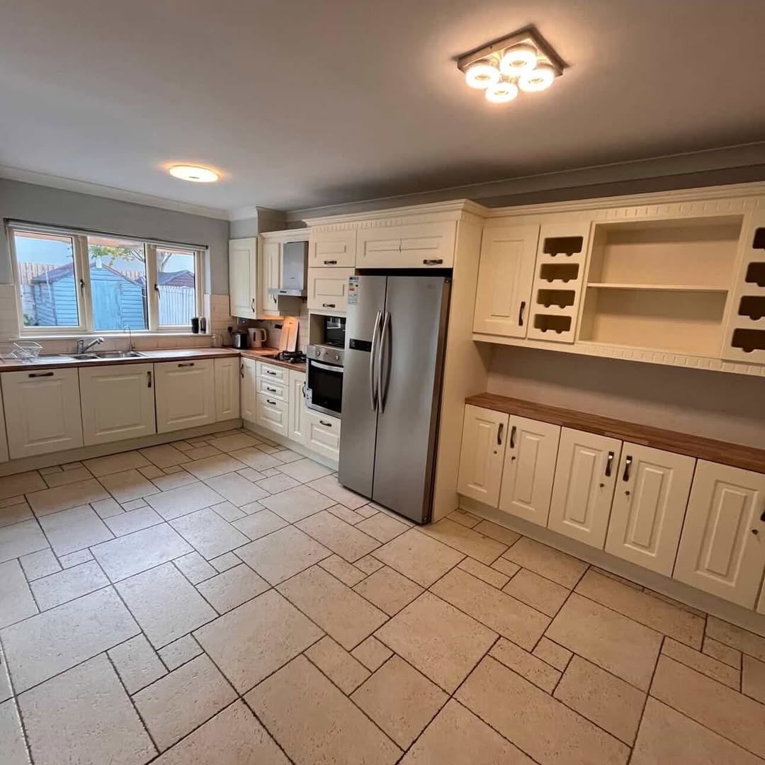 Bright kitchen with cream cabinets, stainless steel fridge, and tile flooring.