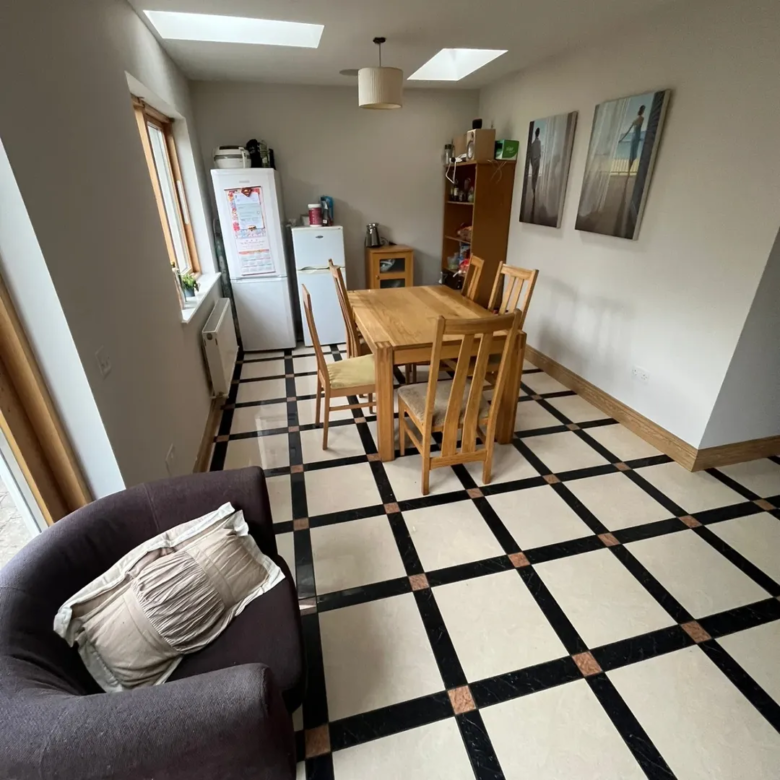 Bright kitchen dining area with table, chairs, fridge, and black and cream tiled floor.