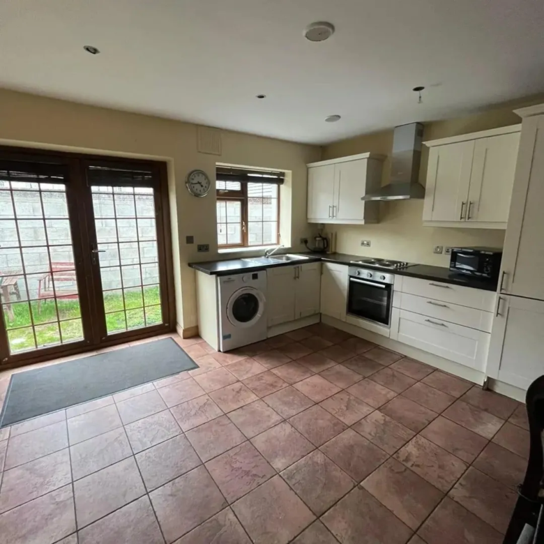 Bright kitchen with white cabinets, washing machine, oven, and view to garden through glass doors.